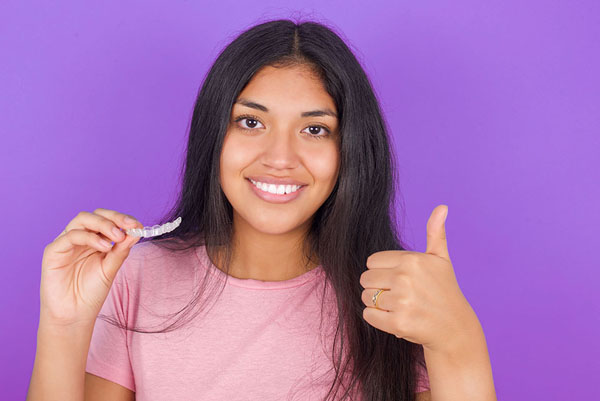 young girl giving a thumbs up while holding her Invisalign clear aligner